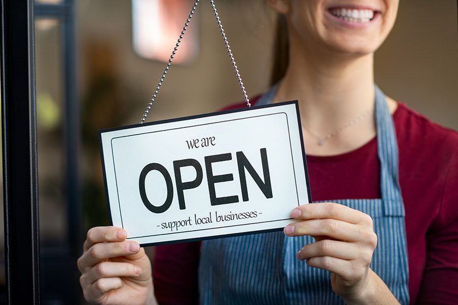 Business Insurance - Smiling Small Business Owner Holding Up Open Sign on Front Door